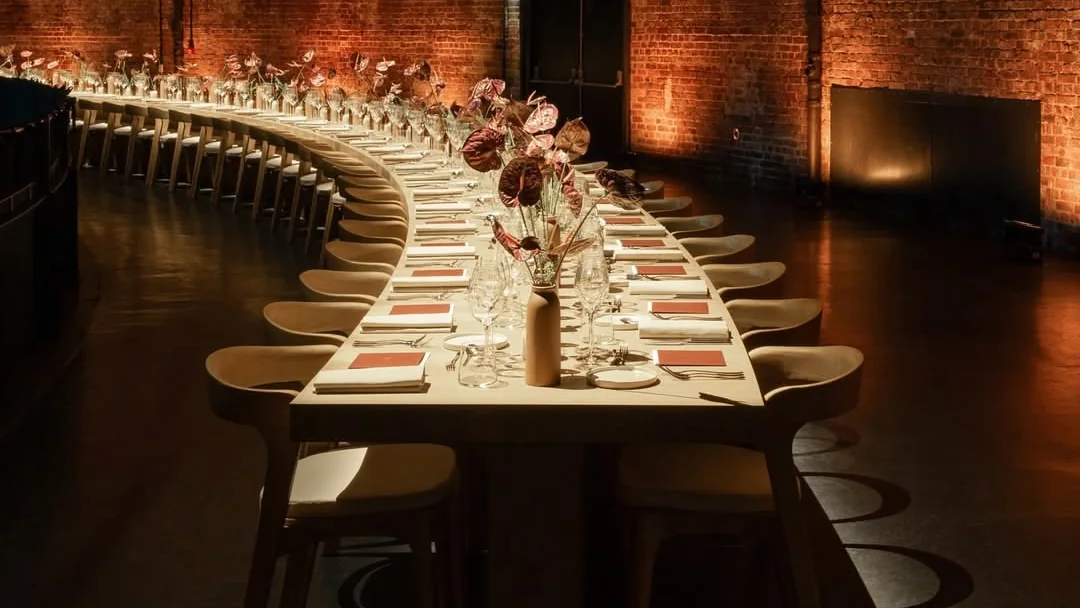 Longue table courbe dressée dans une halle en briques, avant l’arrivée des convives