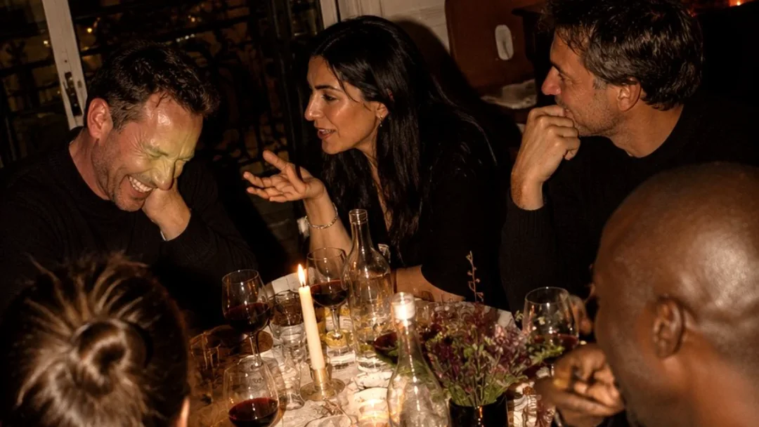 Cinq personnes rient et discutent autour d’un dîner aux chandelles dans un appartement parisien