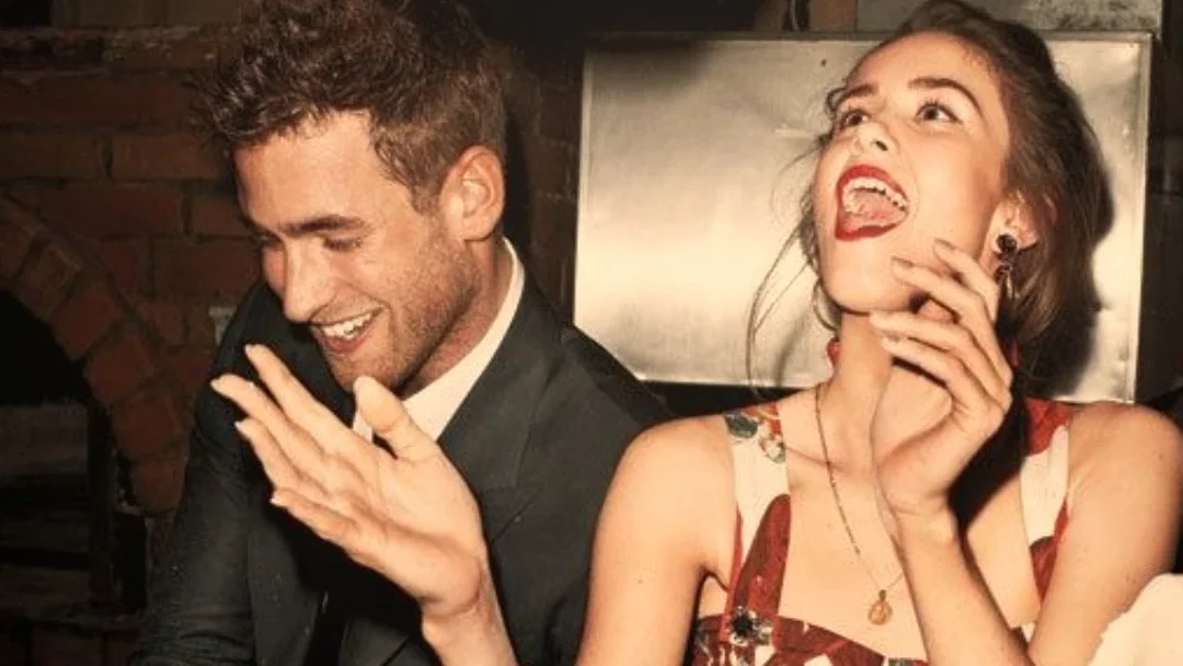Un homme et une femme éclatent de rire en préparant des pizzas devant un four à bois