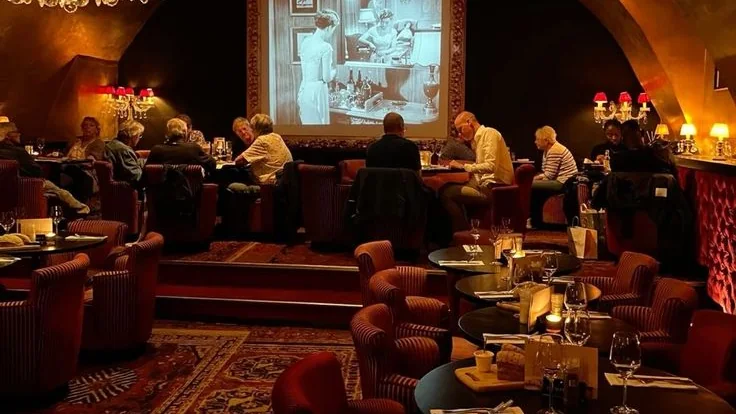 Salle de restaurant feutrée avec fauteuils rouges et projection de film en noir et blanc