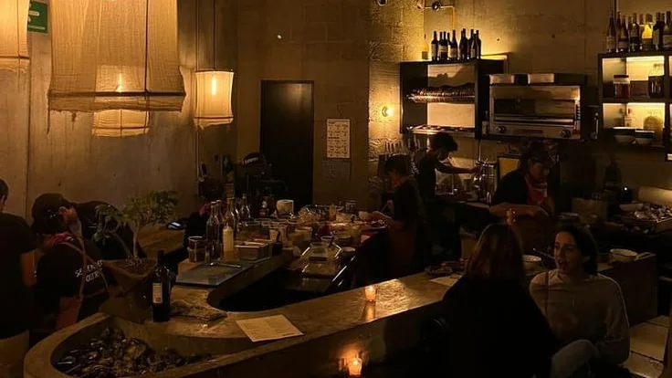 Bar en béton éclairé à la bougie en fin de soirée, quelques clients isolés au comptoir